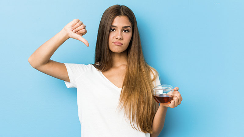 image shows a beautiful woman holding a cup of tea and giving the thumbs down